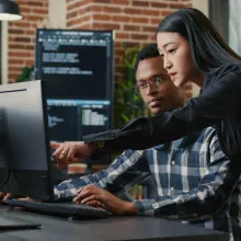 A woman pointing out something on her colleague's monitor screen in a modern office setting
