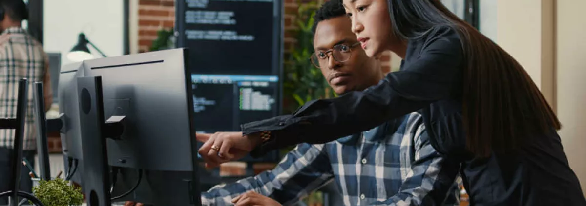 A woman pointing out something on her colleague's monitor screen in a modern office setting